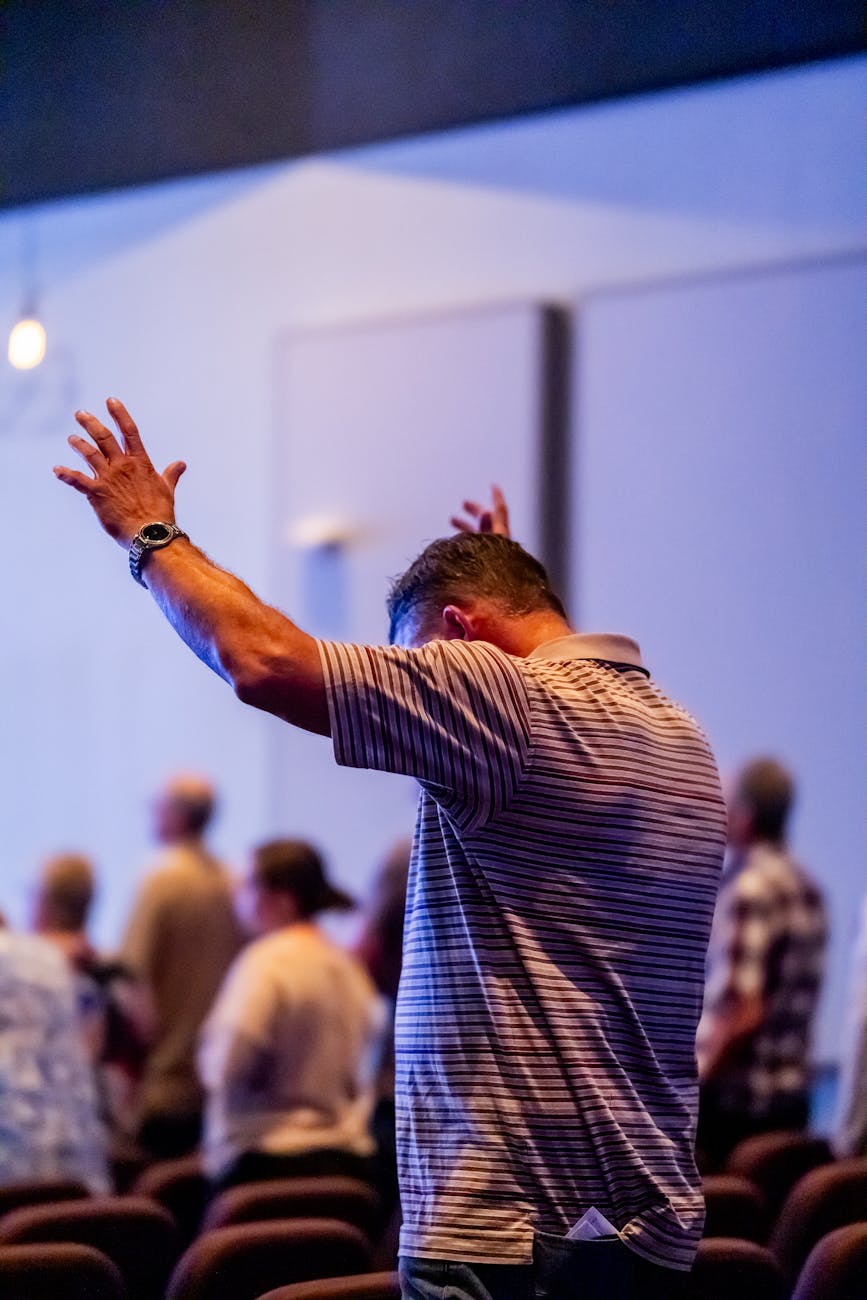 man raising arms in worship at church service