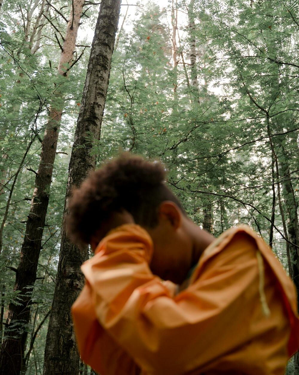 teenage boy in yellow raincoat with head in hands in forest