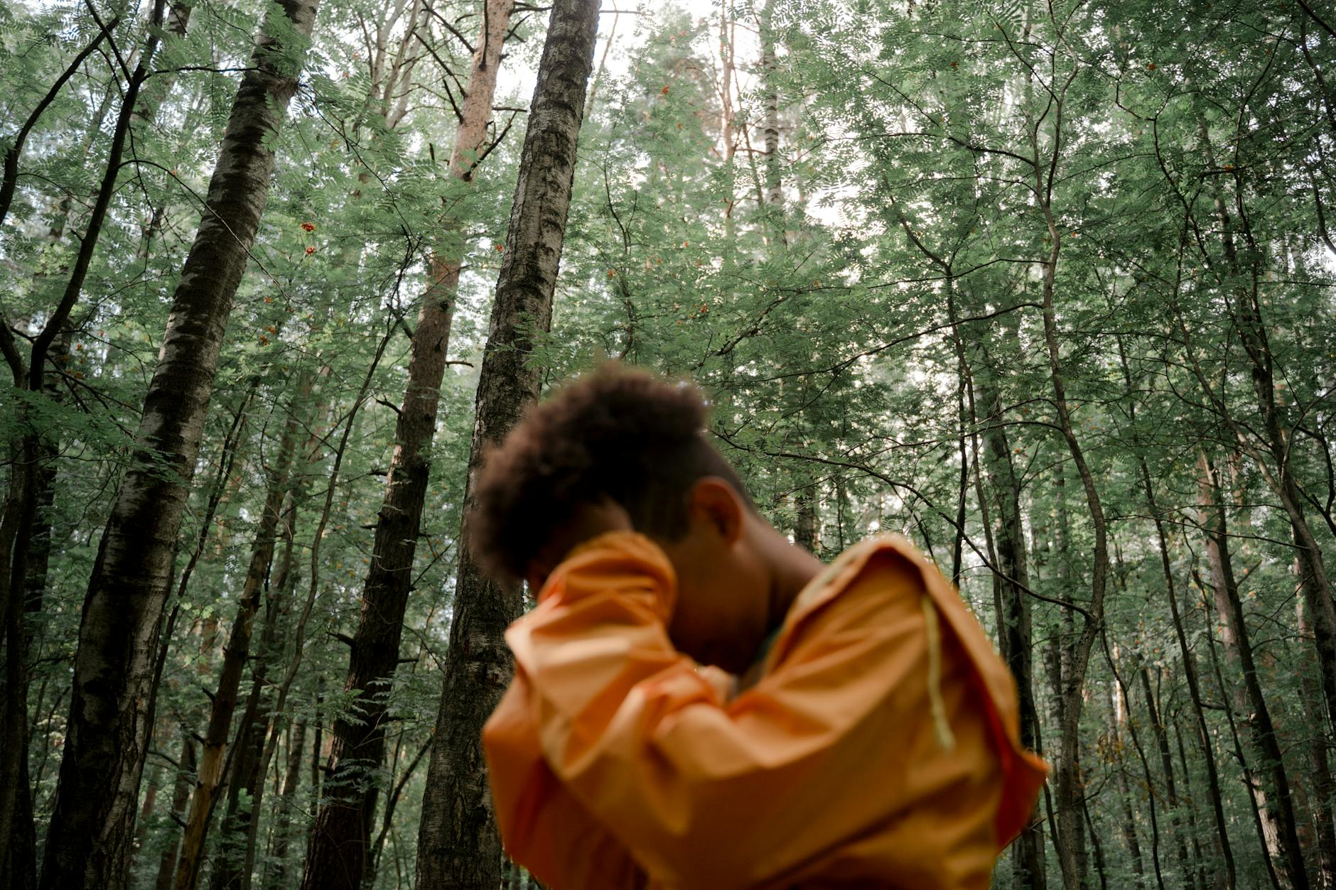 teenage boy in yellow raincoat with head in hands in forest