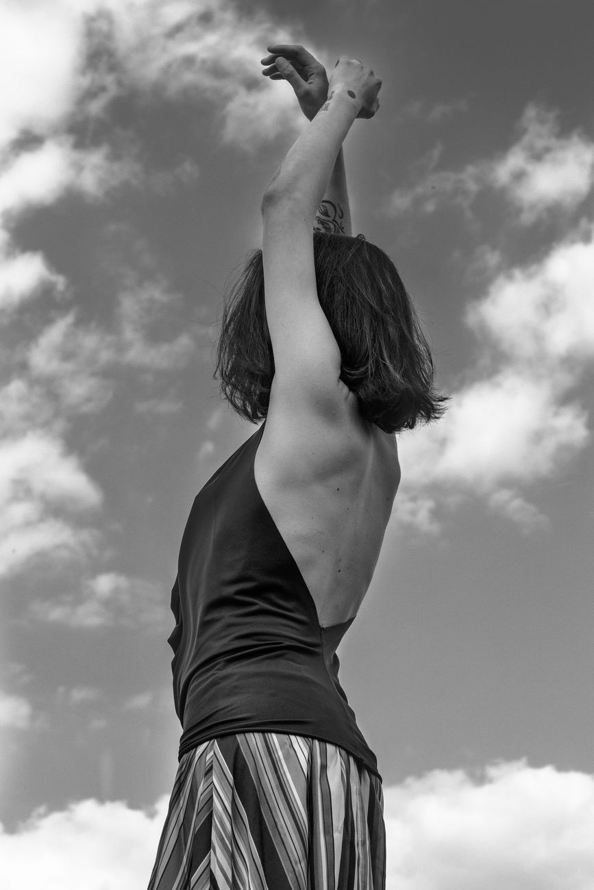 anonymous female dancer raising hands against cloudy sky