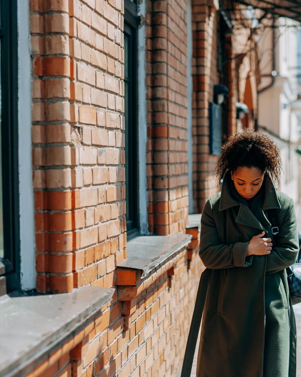woman in brown coat standing near brown brick wall
