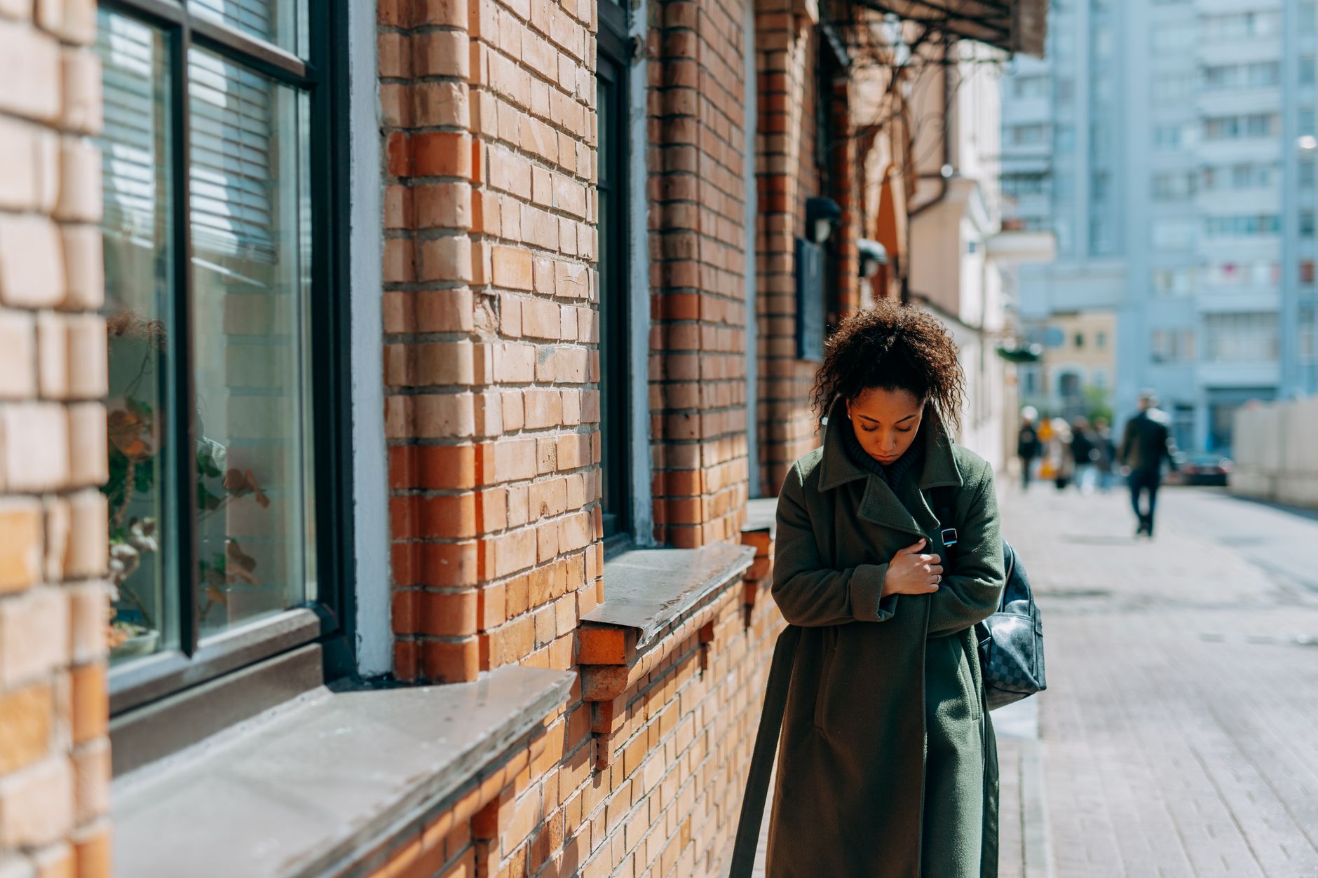woman in brown coat standing near brown brick wall